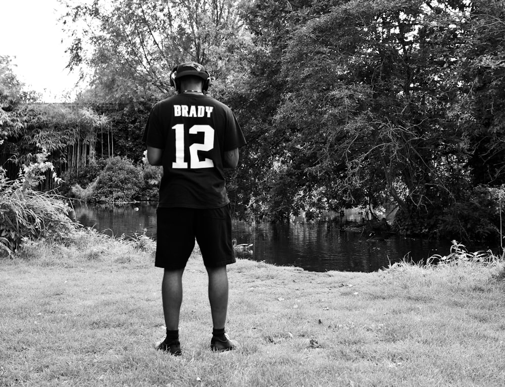 grayscale photo of man in black and white jersey shirt and shorts standing on grass field