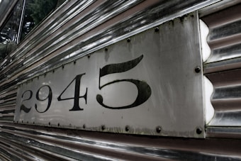 A close-up of the side of a metallic vehicle, displaying the numbers 2945 on a rectangular panel. The surface is made of polished metal with horizontal grooves, and the numbers are prominently displayed in bold black font.