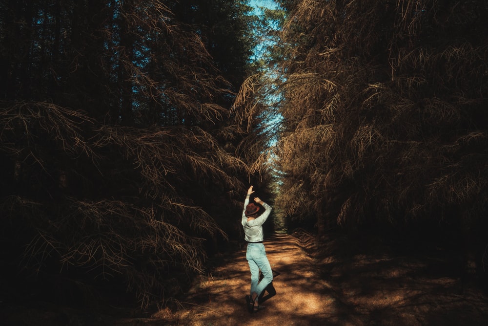 woman in white long sleeve shirt and blue denim jeans standing on brown dried leaves during