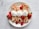 A white plate holds four crepes filled with whipped cream and garnished with fresh strawberries and raspberries. Each crepe is topped with a dollop of whipped cream, and additional berries are placed around the crepes for decoration. The backdrop is a light, marble-textured surface.