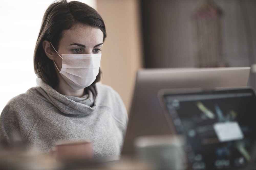 donna in felpa con cappuccio grigia che indossa una maschera facciale bianca