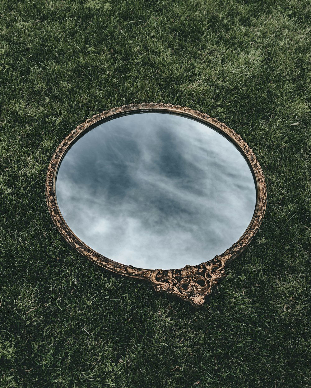 oval mirror with brown wooden frame on green grass