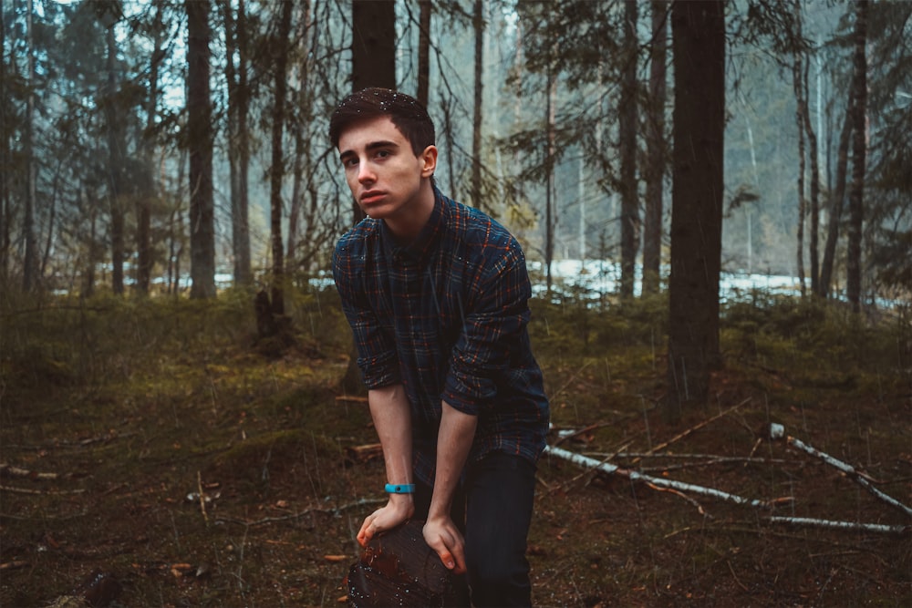 man in black and gray plaid dress shirt and blue denim jeans standing on forest during