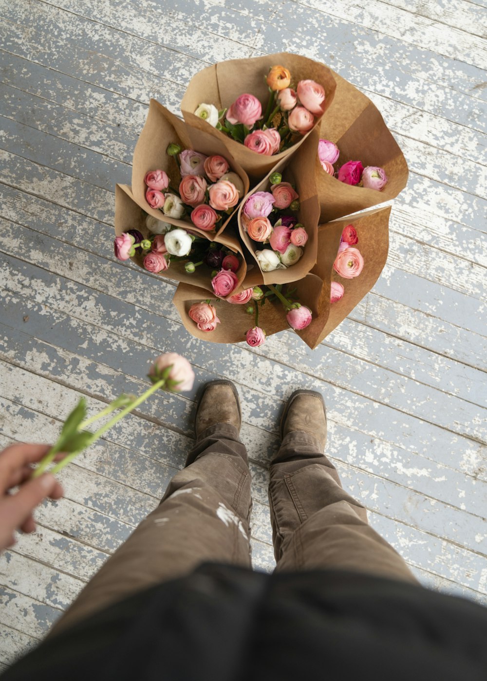 Persona con pantalones marrones y botas marrones con flores rosas en el regazo