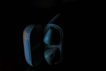 A pair of wireless earbuds inside their open charging case is set against a dark background. The lighting accentuates the sleek, modern design of the earbuds and the reflective surface of the case.