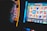 A person is closely observing a digital slot machine with colorful fruit symbols, bars, and a bell. The slot machine screen displays symbols like oranges, plums, cherries, and clouds. The background is dimly lit, creating a focused and somewhat intense atmosphere.