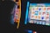 A person is closely observing a digital slot machine with colorful fruit symbols, bars, and a bell. The slot machine screen displays symbols like oranges, plums, cherries, and clouds. The background is dimly lit, creating a focused and somewhat intense atmosphere.
