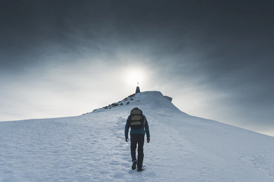 A determined man climbing a steep mountain trail at sunrise, symbolizing spiritual challenges.