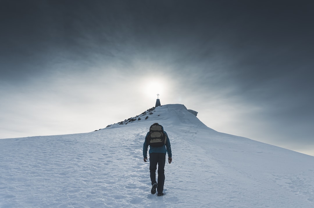 person in black jacket and black pants standing on snow covered ground under gray sky,