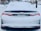 A snow-covered car parked on a residential street, with snow blanketing the rear windshield and trunk, partially obscuring the car's logo and license plate.