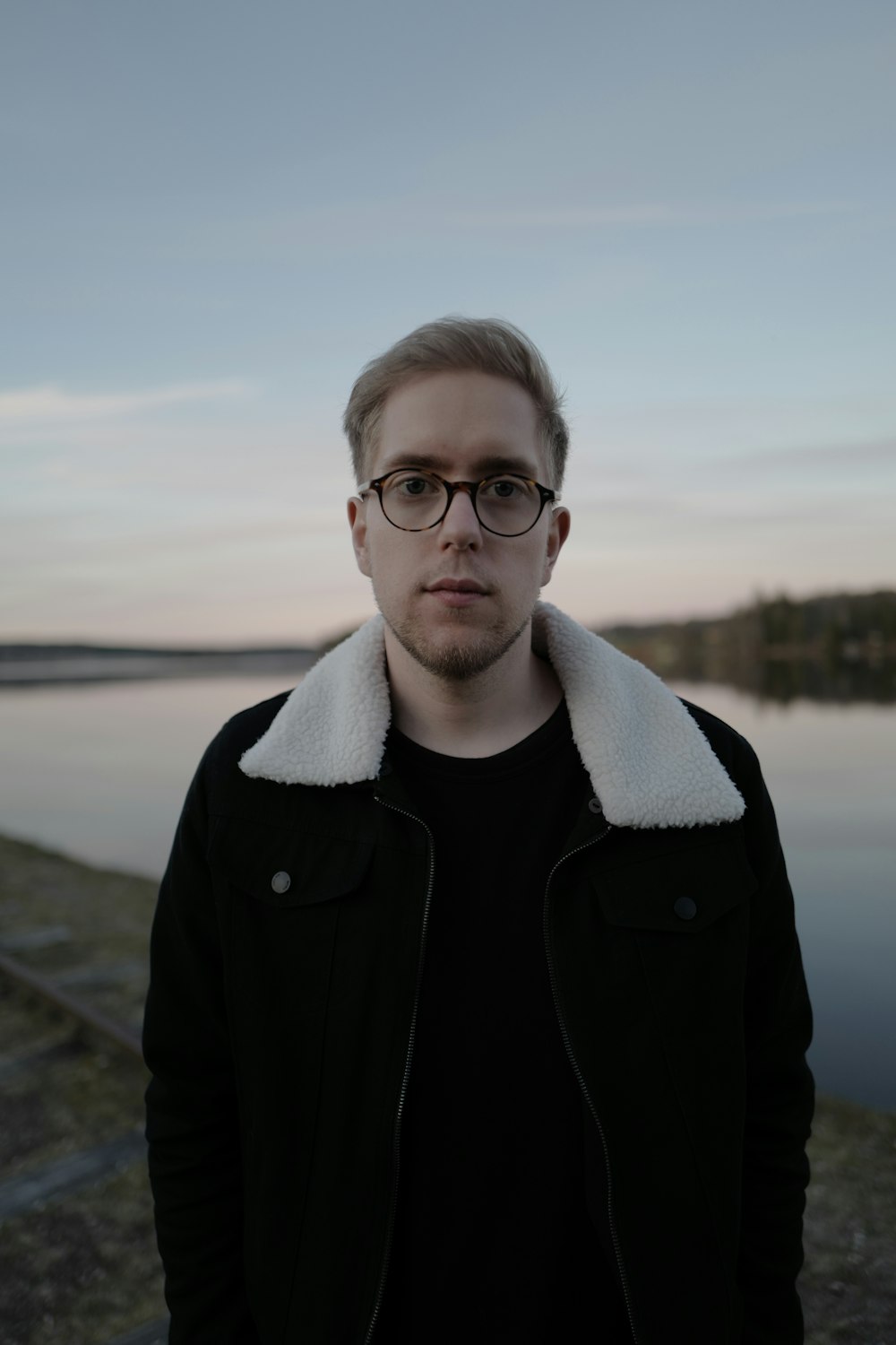 man in black jacket wearing white scarf and black framed eyeglasses