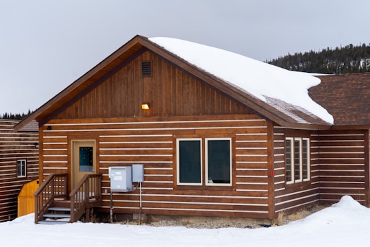 A compact prefabricated cottage nestled on a snow-covered hillside with a sturdy steel frame and sloped roof.
