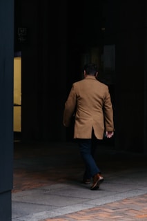 man in brown suit jacket and blue denim jeans standing on brown wooden floor