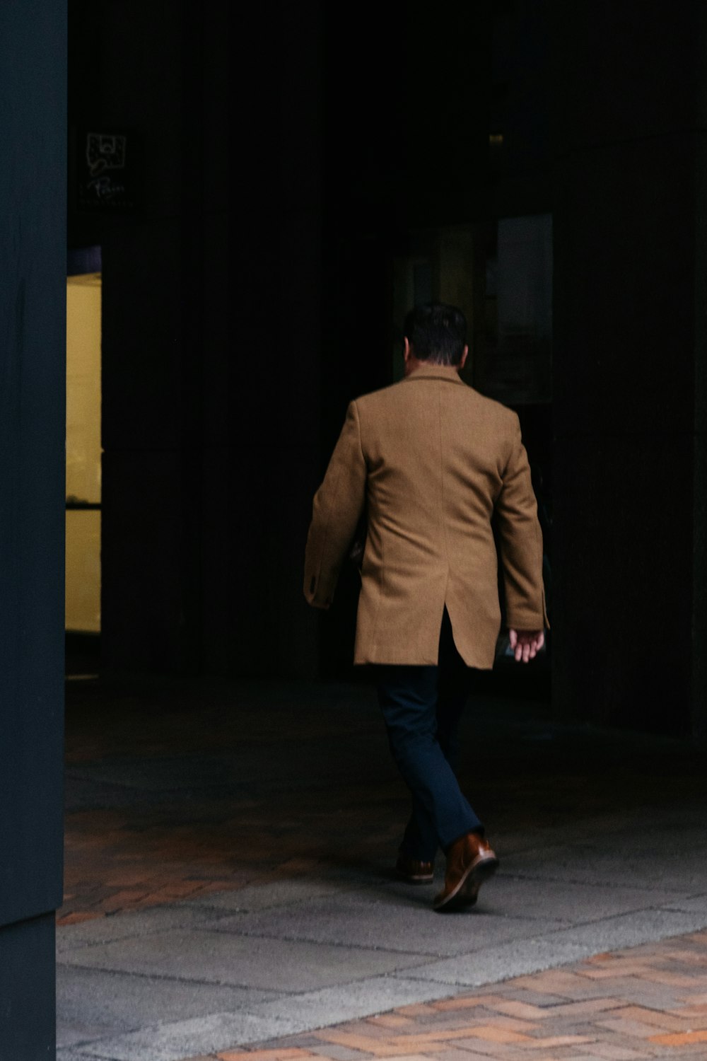 Hombre con chaqueta de traje marrón y jeans de mezclilla azul de pie sobre piso de madera marrón