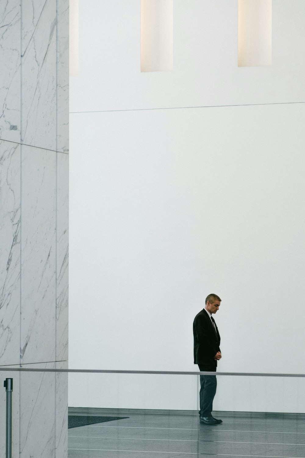 검은 재킷을 입은 남자가 흰 콘크리트 벽 옆에 서 있다