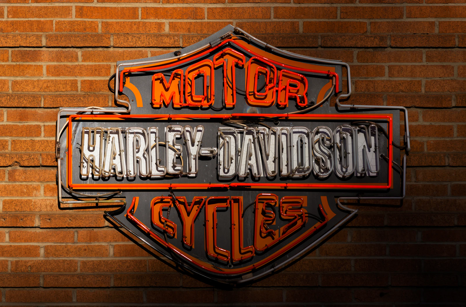 Harley-Davidson bar-and-shield neon sign on a brick wall, for the aftermarket Harley parts Kings North Coast Customs sells through WPS
