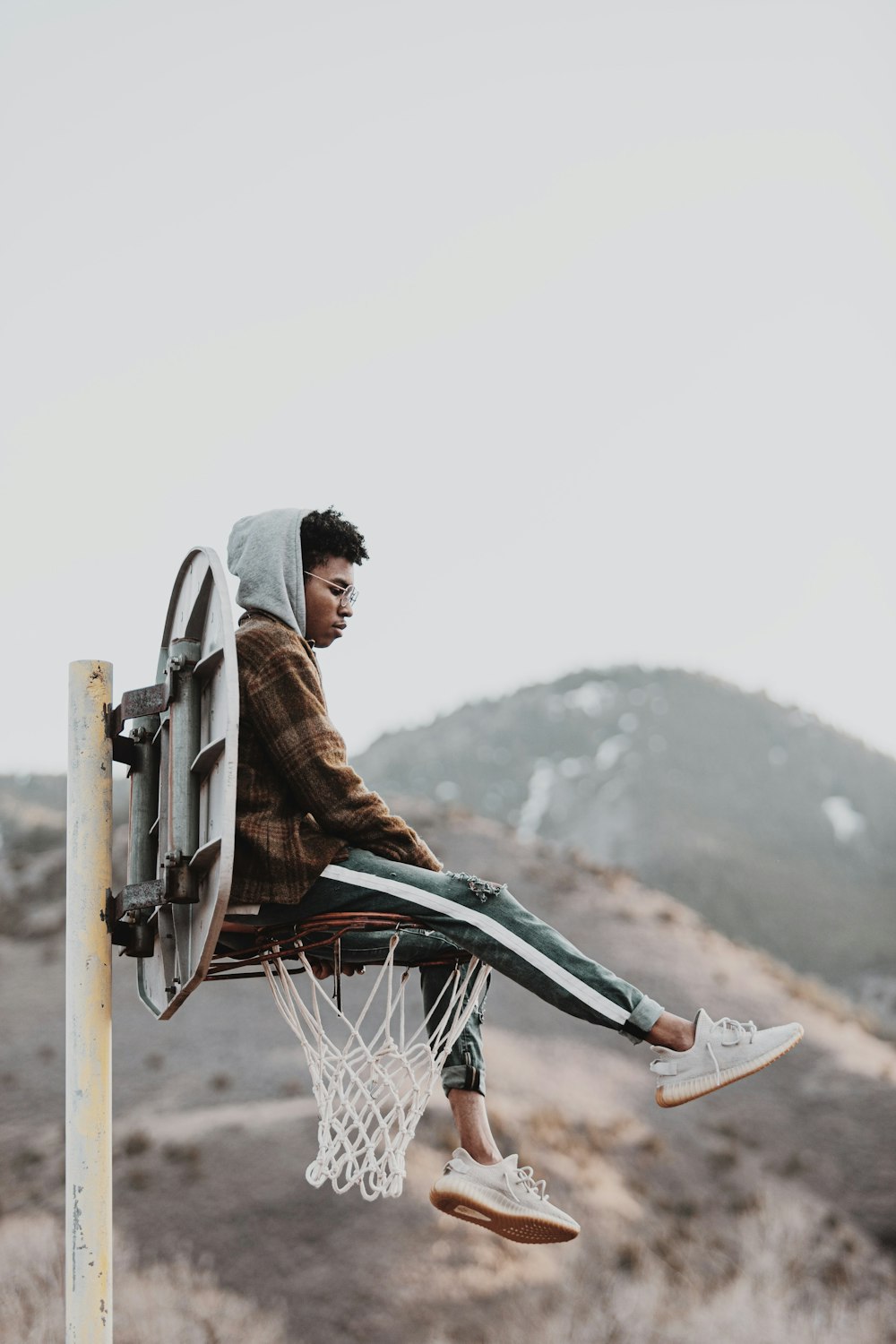 man in brown jacket sitting on brown wooden post during daytime