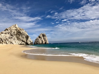 brown rock formation on sea shore under blue sky and white clouds during daytime