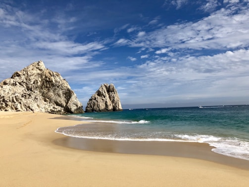 brown rock formation on sea shore under blue sky and white clouds during daytime