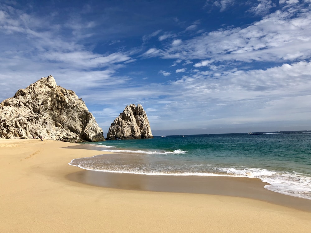 brown rock formation on sea shore under blue sky and white clouds during daytime