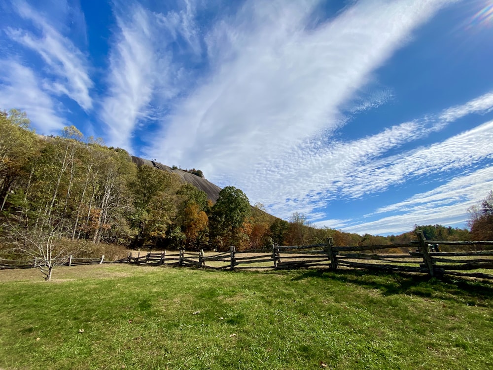 brown wooden fence on green grass field near green mountain under blue sky during daytime