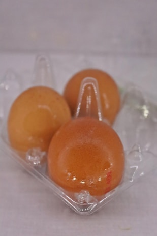 Three brown eggs rest inside a transparent plastic egg carton against a plain background.
