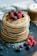 A close-up of a stack of golden soufflé pancakes topped with fresh berries and a drizzle of syrup.