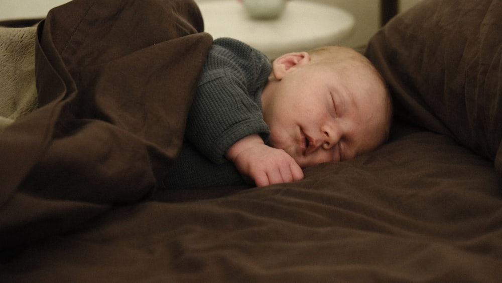 baby in gray sweater lying on brown textile