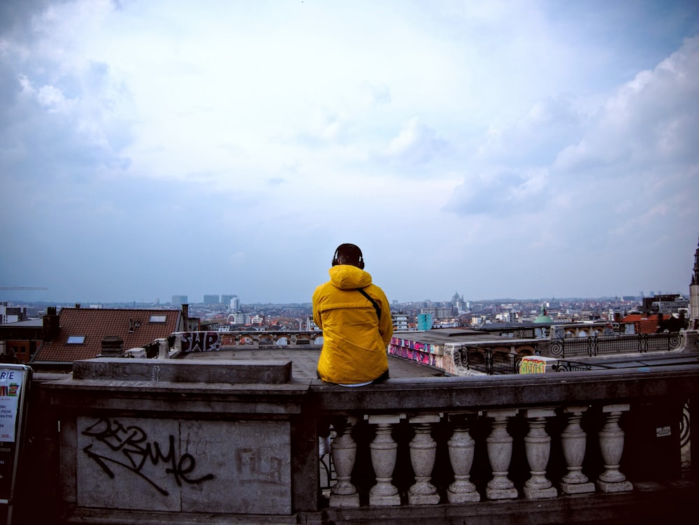 man in yellow hoodie sitting on brown concrete fence during daytime