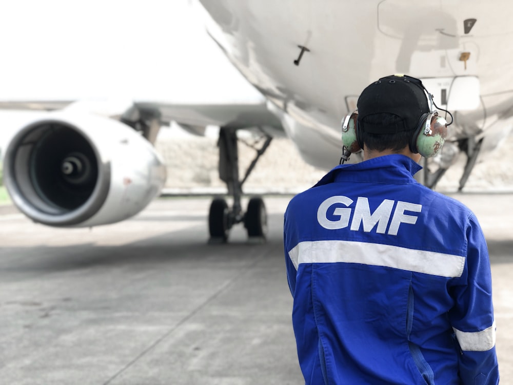 man in blue and white jacket standing near white airplane