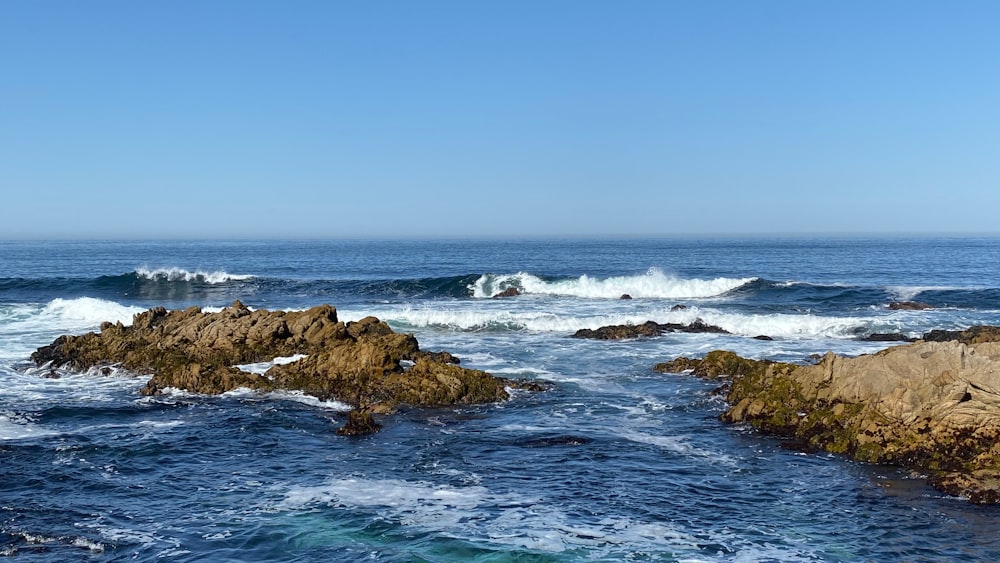 formação rochosa marrom no mar sob o céu azul durante o dia