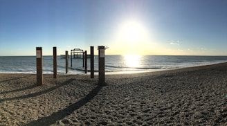the sun is setting on a beach with a pier in the distance