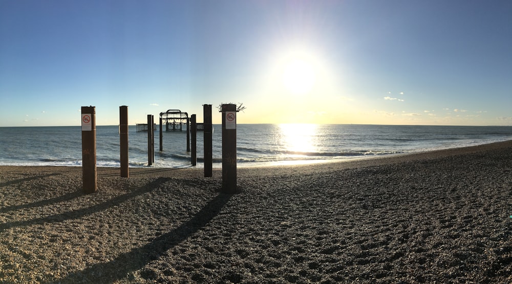 the sun is setting on a beach with a pier in the distance