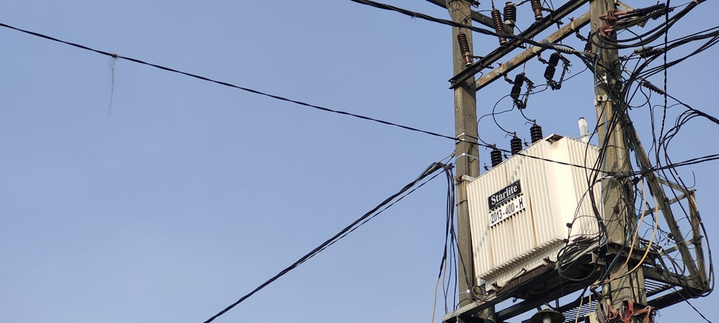 A utility pole with numerous electrical wires is visible, featuring a large transformer labeled 'Starlite' mounted on a metal structure. The sky in the background is clear and blue.