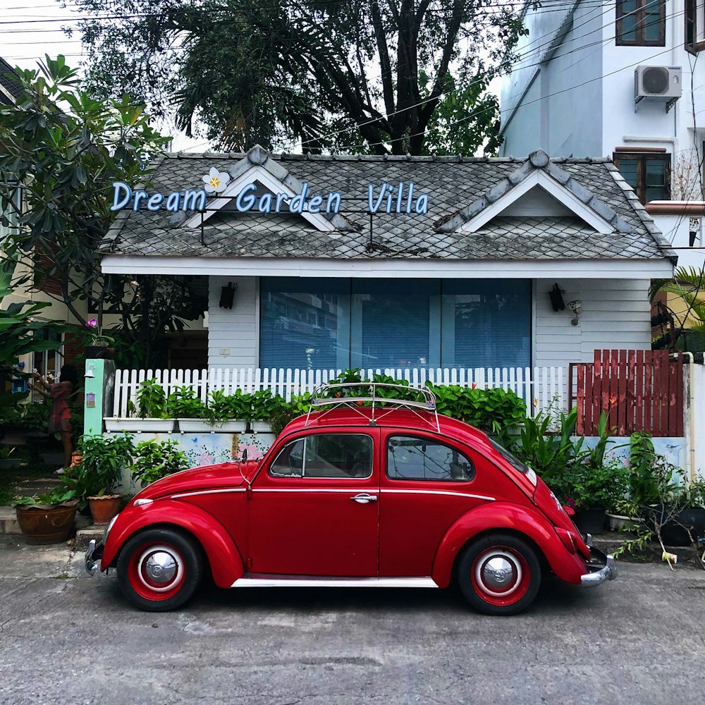 red volkswagen beetle parked beside white wooden fence
