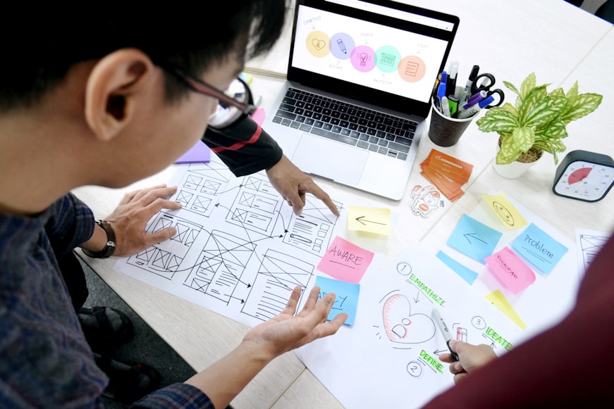 UI UX designer having a discussion about product prototype with multiple sticky notes and infographics in working environments.