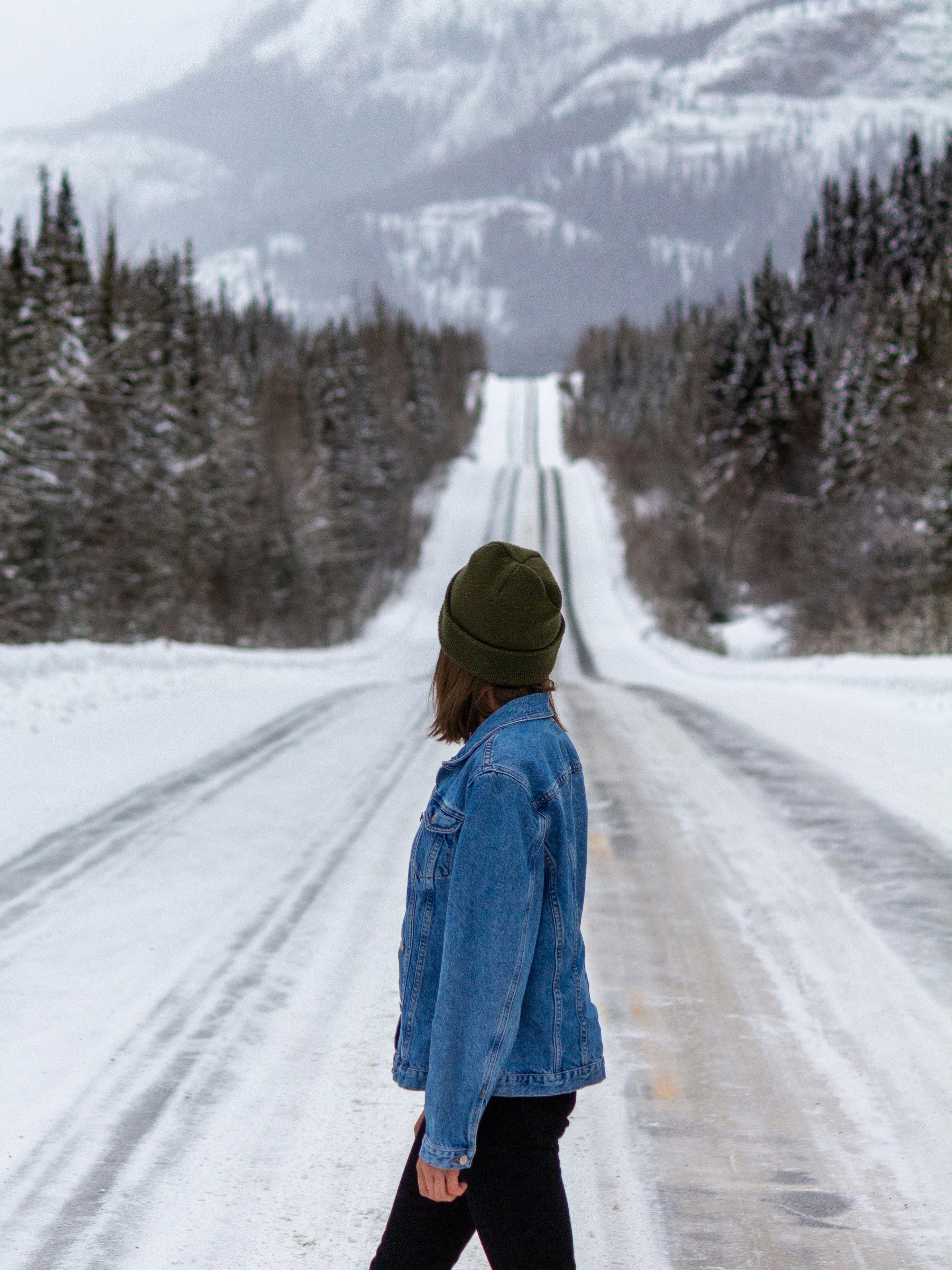 woman in blue coat walking on snow covered road during daytime