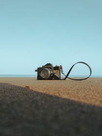 A close-up of a vintage camera resting on a sandy surface with seashells scattered nearby, capturing the essence of travel memories.