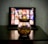 A glass jar filled with popcorn is placed on a dark wooden table. In the background, there's a blurred image of a tablet or screen displaying a grid of colorful thumbnails, suggesting a streaming service interface.
