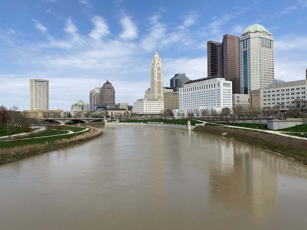 body of water between green grass field and city buildings during daytime