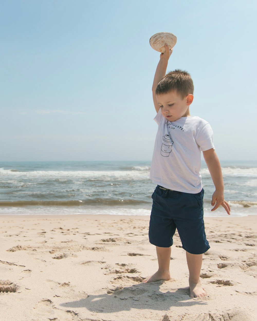 boy in white t-shirt and blue shorts standing on beach during daytime