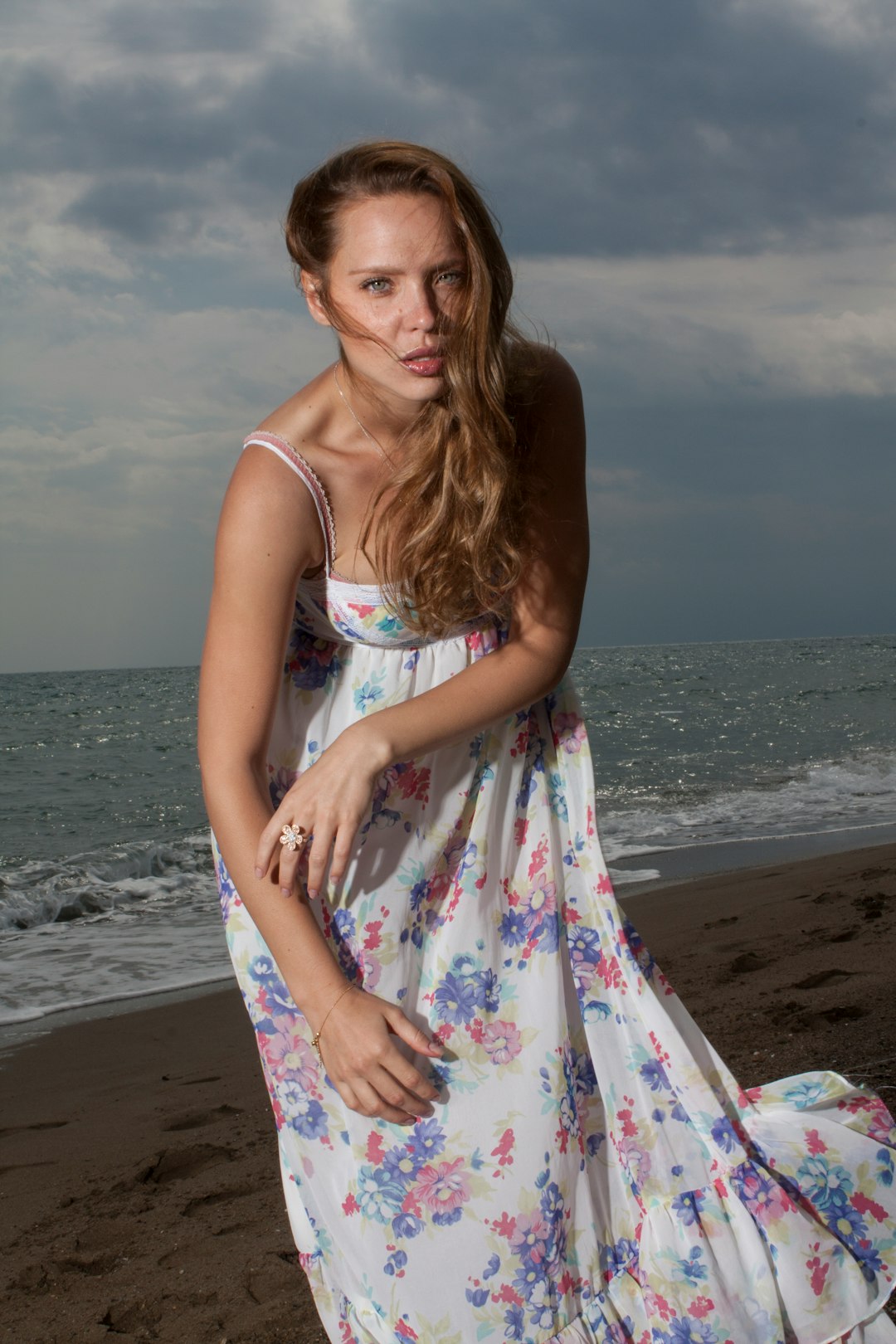 woman in white blue and pink floral spaghetti strap dress standing on beach during daytime