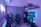 A modern gaming setup featuring a sleek gaming chair, dual monitors on a desk, and LED lighting. A gaming console and various decorations are displayed on shelves, creating an organized and vibrant gaming environment.