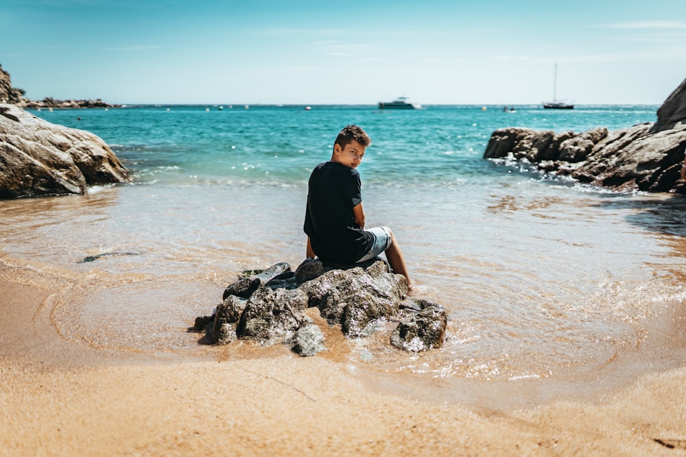 man in black shirt sitting on brown sand near body of water during daytime
