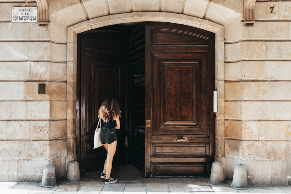 woman in black dress standing beside brown wooden door