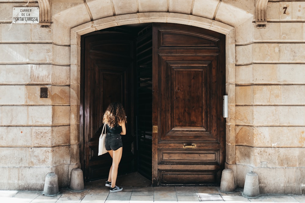 mujer con vestido negro de pie junto a la puerta de madera marrón