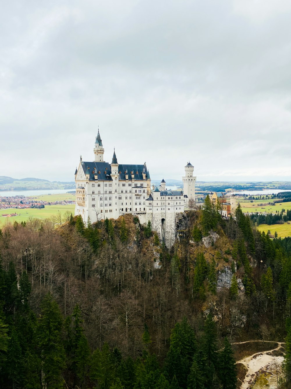 Château blanc et noir entouré d’arbres verts sous des nuages blancs pendant la journée