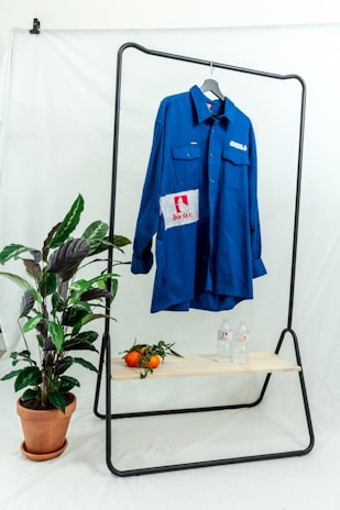 A vibrant close-up of a blue slime-inspired graphic tee hanging on a rustic wooden rack.