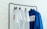 A black clothing rack holds four garments on hangers. Three of the items are white t-shirts with red graphics, and the last one is a blue shirt with a label on the back. The background is a plain white, creating a clean and minimalist look.