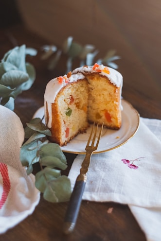 A slice of festive fruit cake with sparkling icing and colorful dried fruits inside.